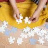 Kinderhände setzen zwei helle Puzzleteile auf einem Holzfußboden zusammen