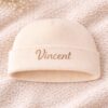 Frontansicht einer cremefarbenen Babymütze mit goldener Stickerei Vincent